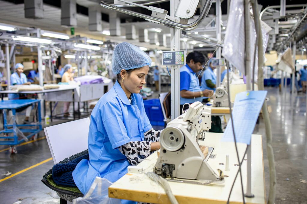 Local Apparel Manufacturing in Kuala Lumpur Workers in a apparel factory operating sewing machines, wearing blue uniforms and hairnets, focused on their tasks.