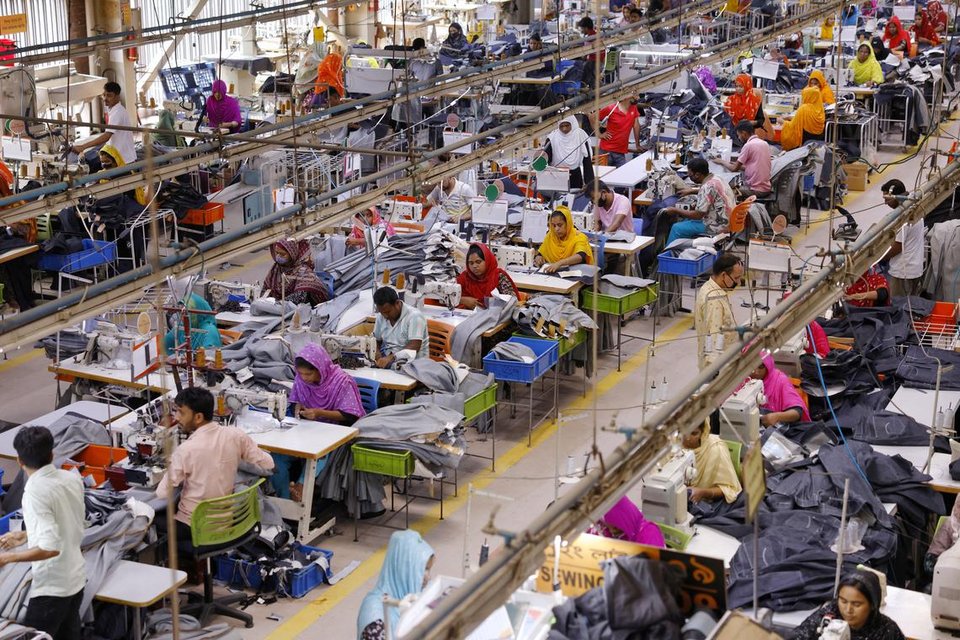 Bangladeshi male and female garment workers sewing clothing in a factory setting.