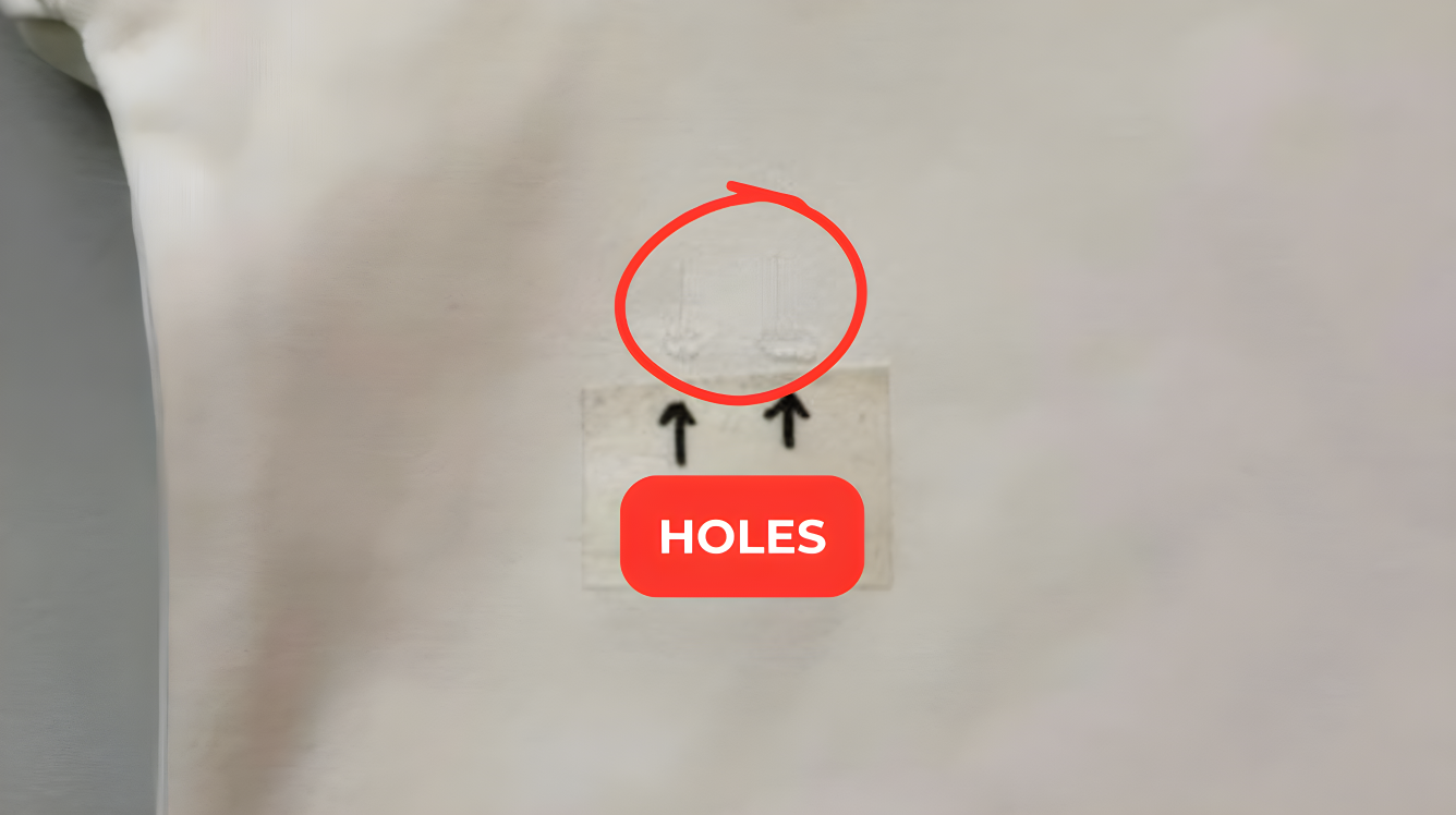 Close-up of fabric or garment with visible holes, inspected by a quality control specialist, marked with a red defect tag.